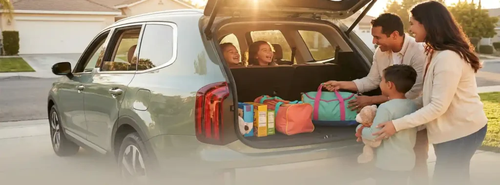 Family loading colorful bags and toys into an SUV trunk on a sunny suburban driveway, kids laughing in the back seat during a road trip morning.