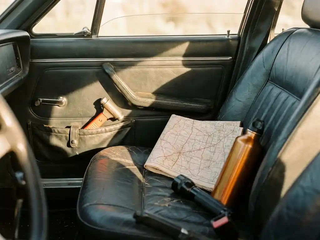 Lifehammer safety hammer clipped to a car door pocket beside a folded map, water bottle, and flashlight on a leather seat.