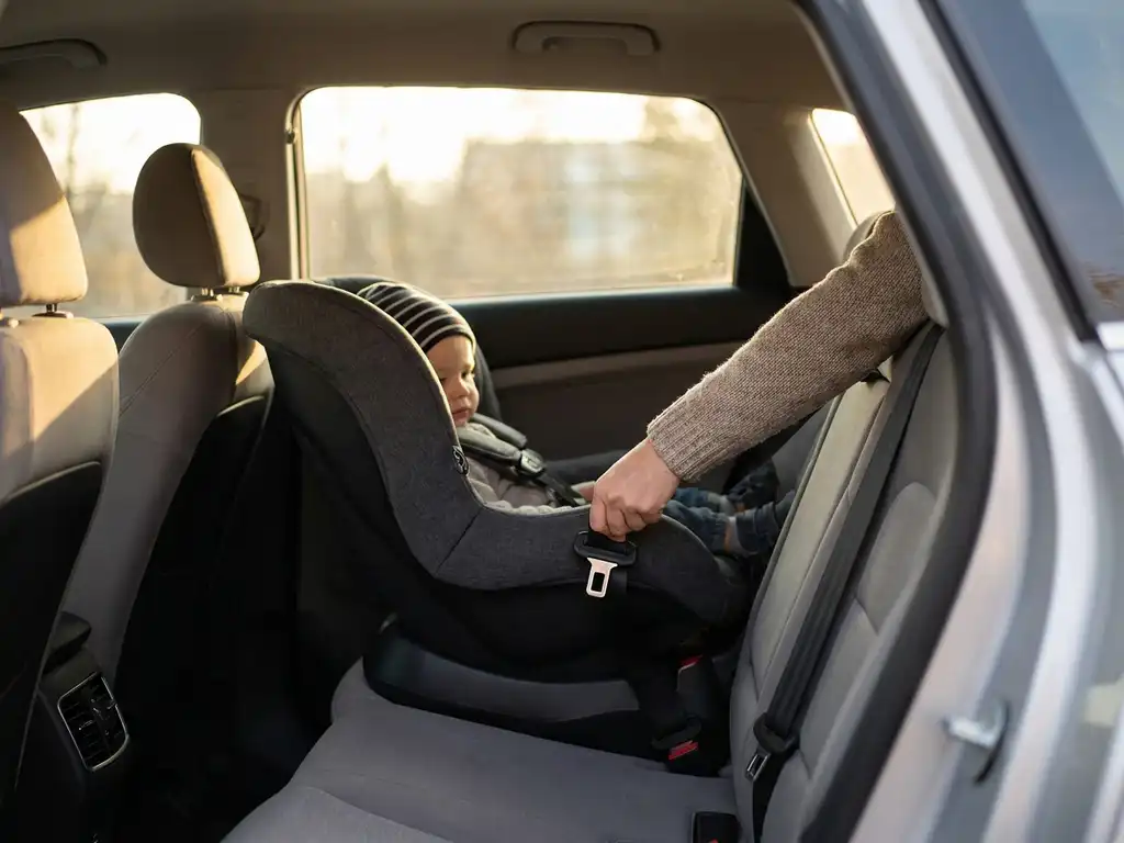 Parent buckling toddler into rear-facing car seat in SUV, warm afternoon light highlighting the seatbelt latch.