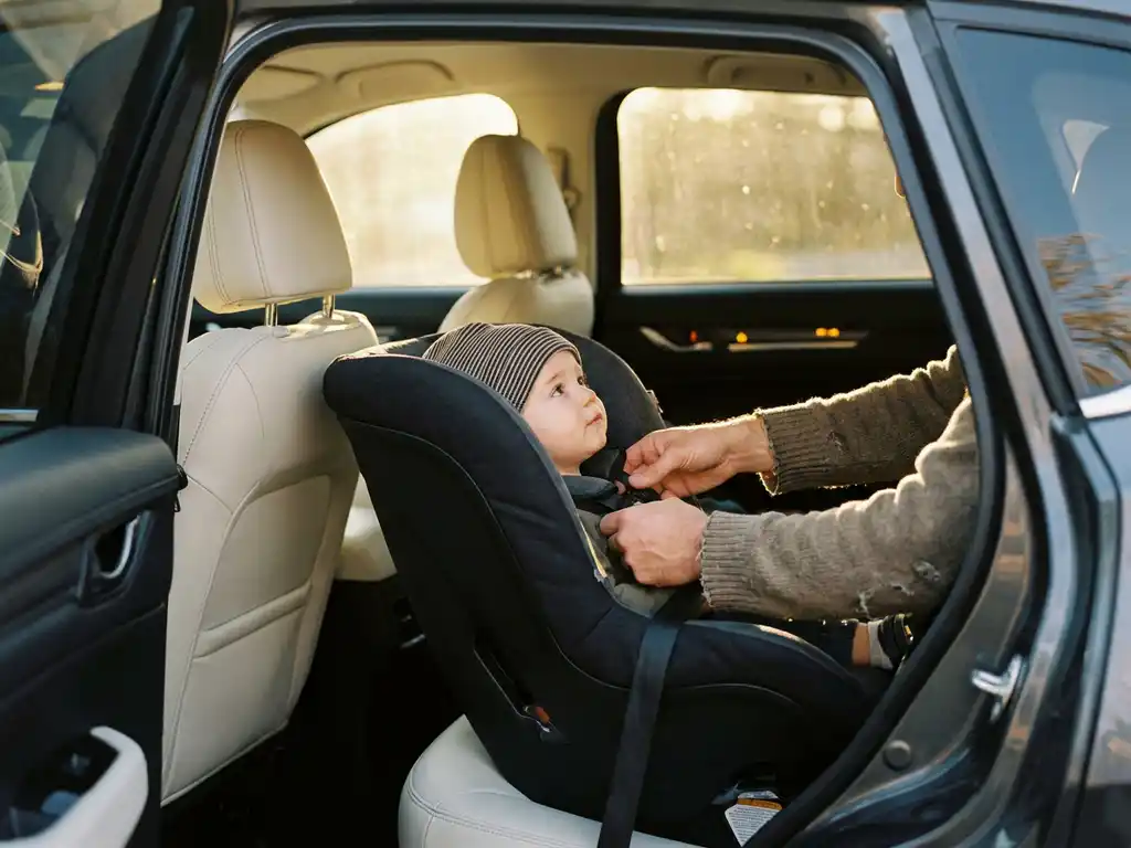 Parent buckling a toddler into a rear-facing car seat in an SUV, checking harness straps in warm afternoon light.